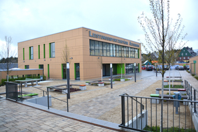 großer Blockbau, im Vordergrund Sitzbänke und kahle Bäume