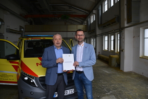 zwei Personen vor ASB Rettungsfahrzeug mit Urkunde