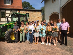 mehrere Personen mit Blumen in der Hand vor einer Scheune und neben einem Traktor