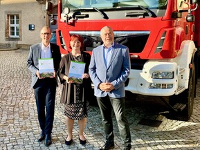 drei Personen vor Fahrzeug mit Mappe