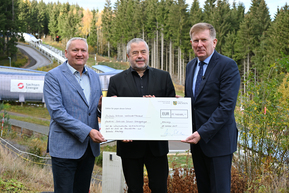 drei Personen vor Bobbahn mit übergroßem Fördermittelbescheid