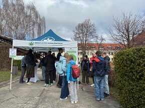 Gruppe an Schülerinnen und Schülern an Informationsstand unter freiem Himmel