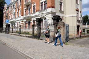 zwei Personen mit Unterlagen gehen zu einem Haus
